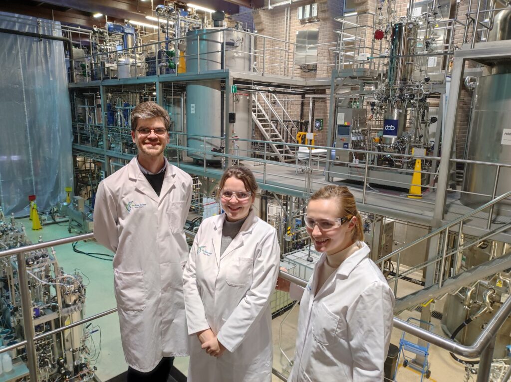 来自GFI欧洲的Alex, Pauline和Ellie站在欧洲生物基地的试验工厂里＂class=
